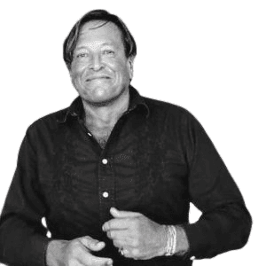 Black and white photo of a man smiling, wearing a dark button-up shirt and bracelets.